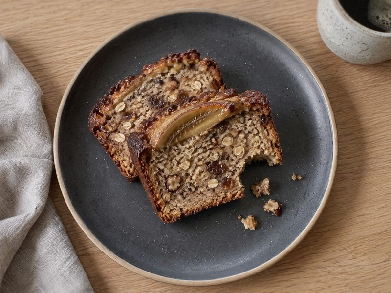 Bananbrød med havregryn og dadler på en mørk tallerken, set ovenfra