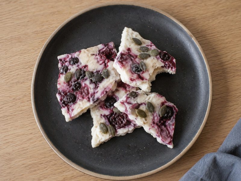 Frossen yoghurt-bark med bær på en mørk tallerken, set ovenfra